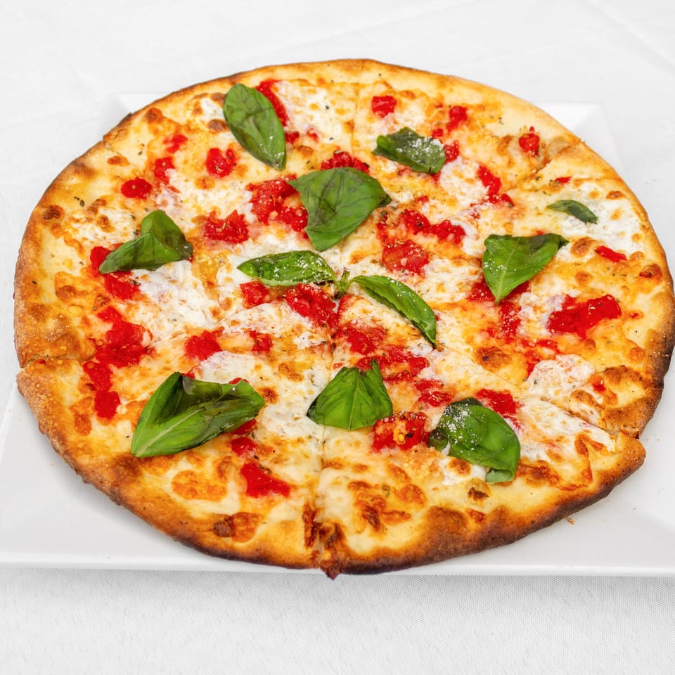 Thin-crust cheese pizza topped with tomato sauce and fresh basil leaves, served on a white square plate.
