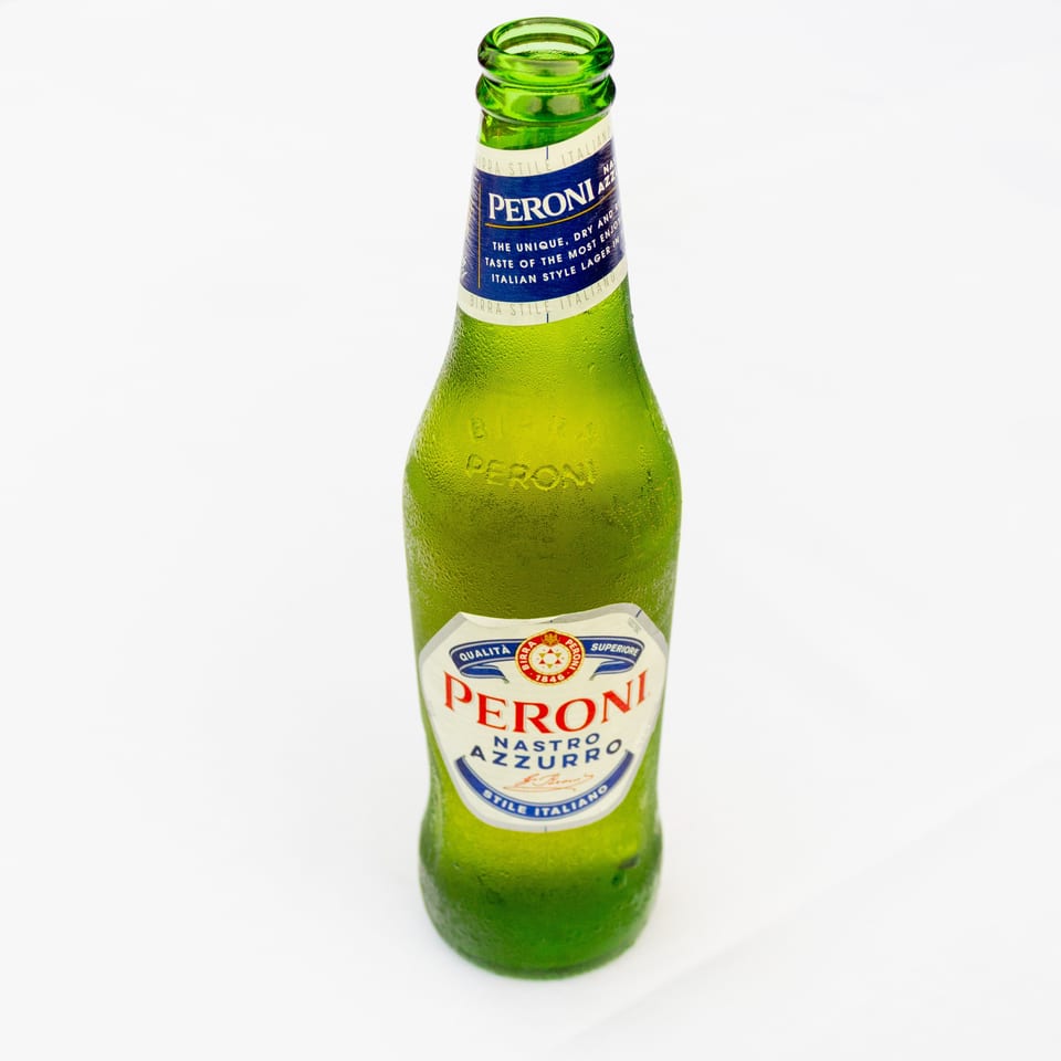 Chilled green Peroni Nastro Azzurro beer bottle standing against a white background.