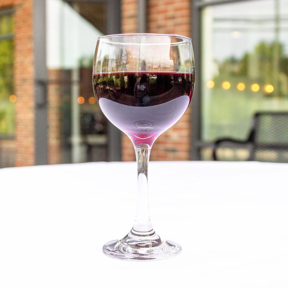 Glass of red wine on a white table overlooking a softly lit restaurant patio.