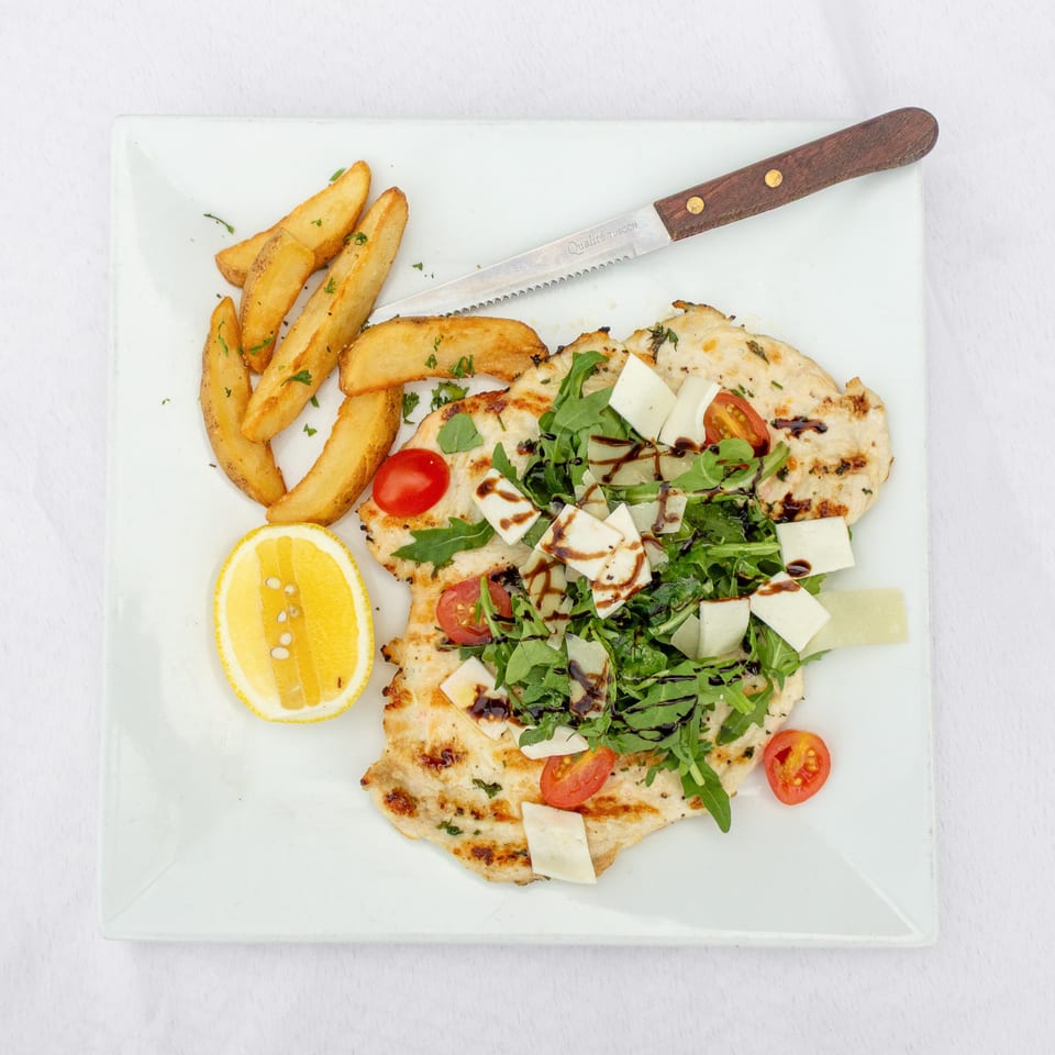 Grilled chicken topped with arugula, tomatoes, cheese, and balsamic glaze, served with potato wedges and lemon.