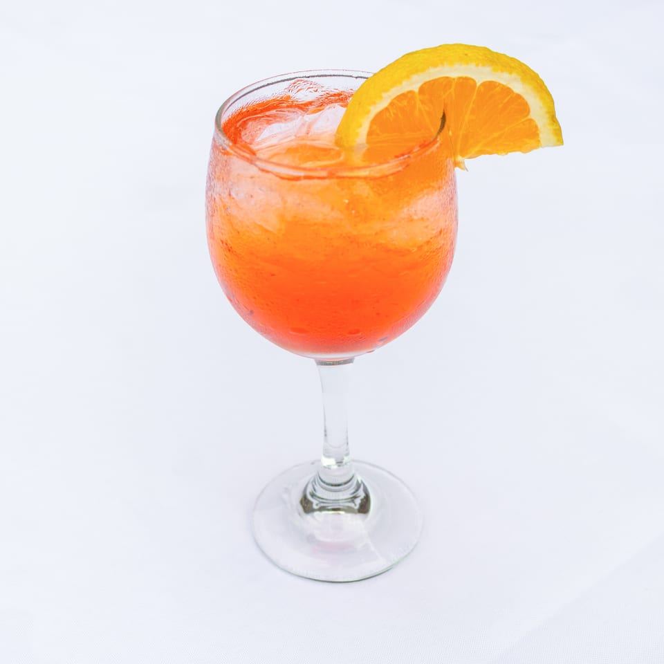 Orange cocktail with ice served in a stemmed glass and garnished with a large orange slice.
