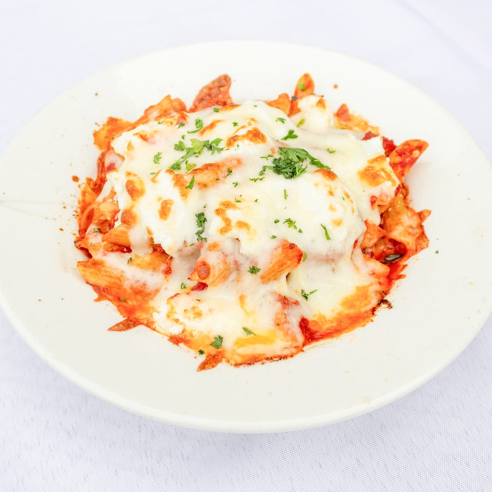 Baked pasta covered with melted golden cheese, tomato sauce, and fresh parsley on a white plate.