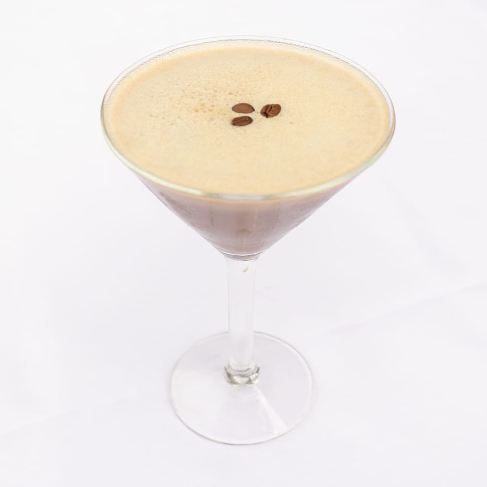Creamy espresso cocktail in a martini glass, topped with three coffee beans against a white background.