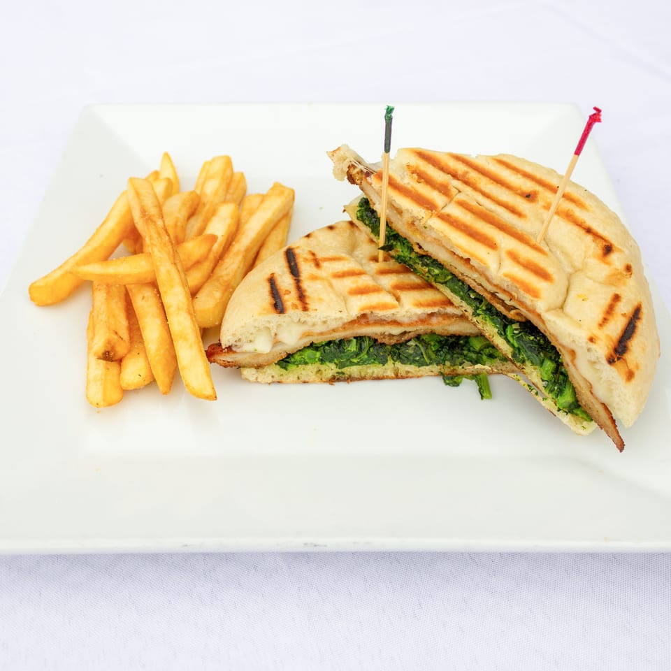 Grilled vegetable panini cut into wedges, served with golden French fries on a white plate.