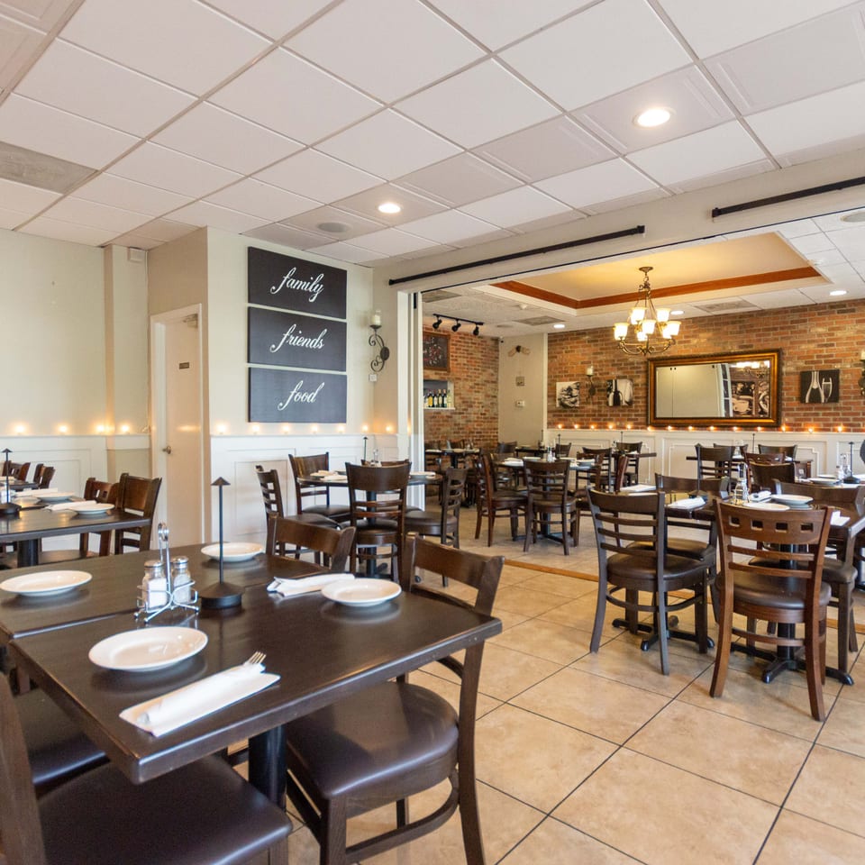 Spacious restaurant dining room with set tables, dark wooden chairs, exposed brick walls, chandelier lighting, and family-friendly decor.